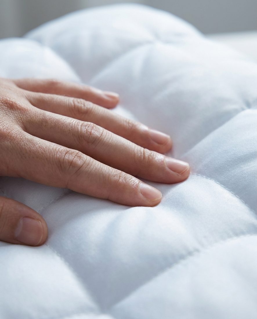 A hand pressing into the cool ice-silk face of the pillow, showing soft loft